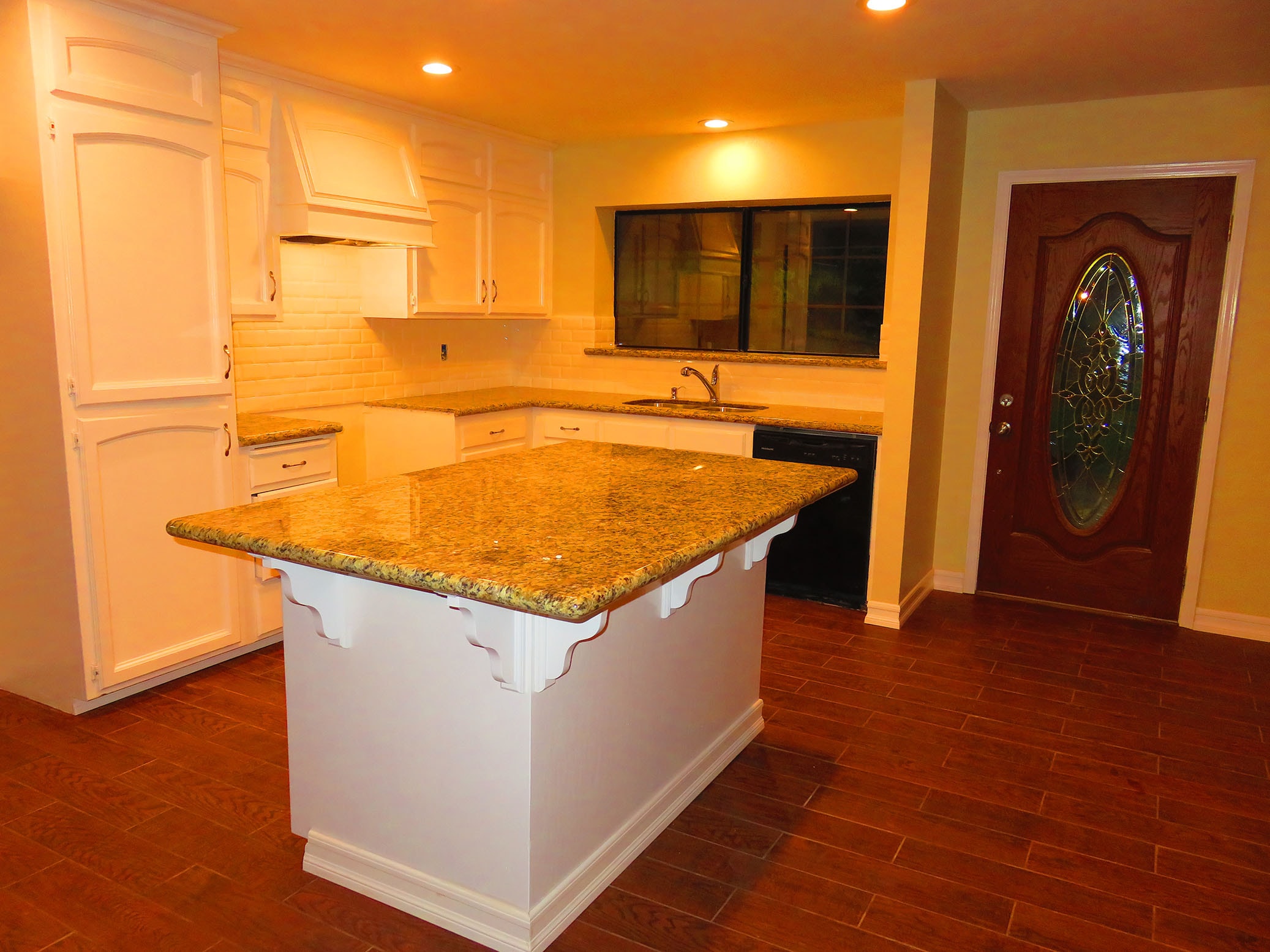 Kitchen remodel with white cabinetry, granite island countertop, and wood-look tile flooring